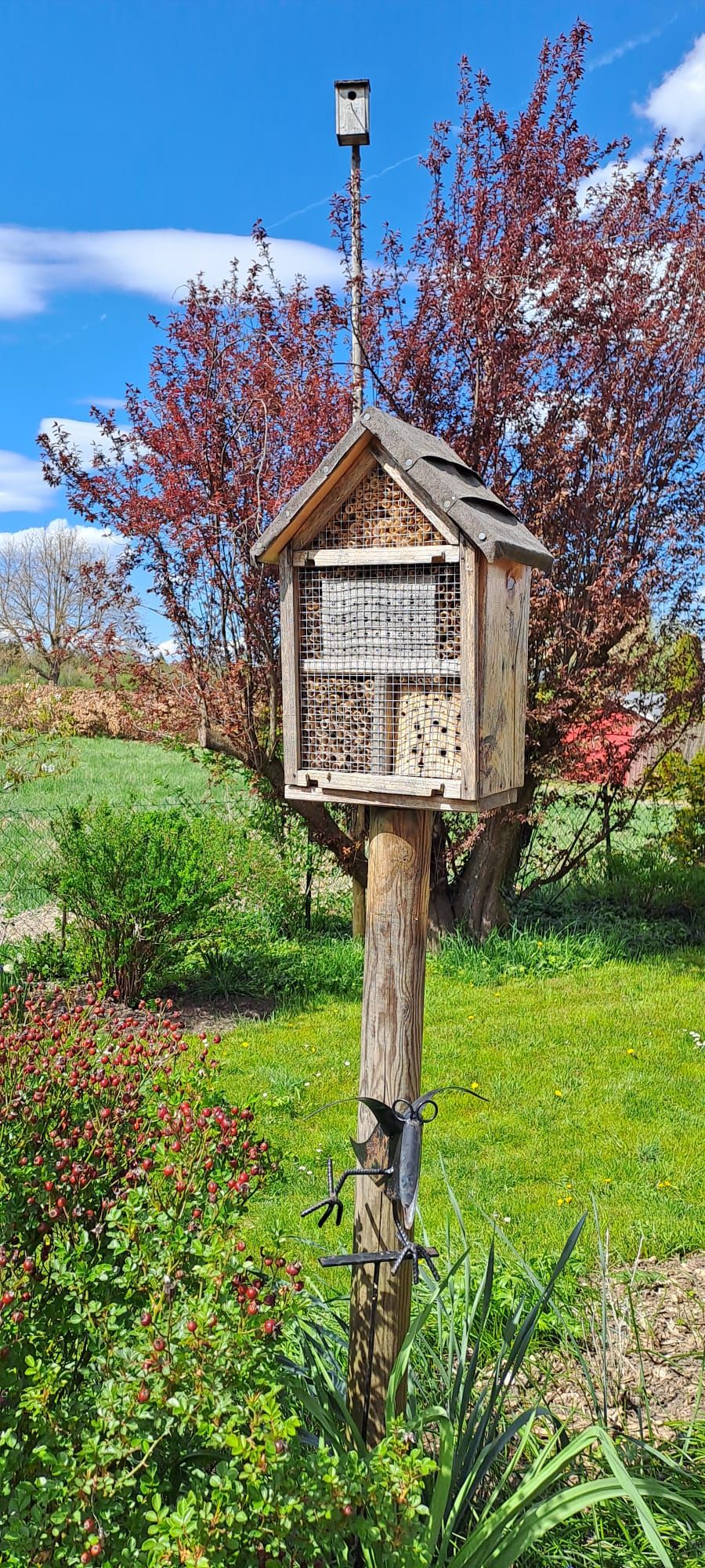 Großes Insektenhotel auf einem Holzpfahl in einem grünen Garten